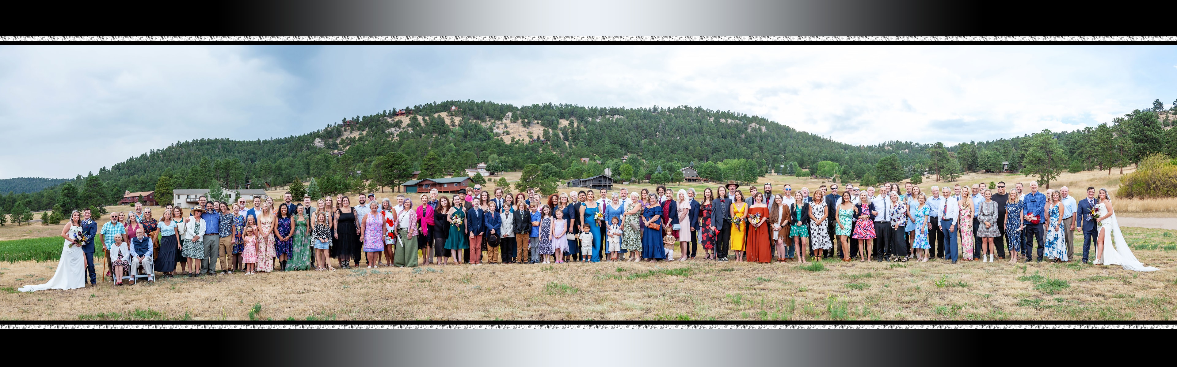 Wedding panoramic photo — large group of guests outdoors with forested hillside backdrop